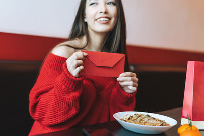 Beautiful young asian woman in red clothes eating asian food with red envelope in restaurant