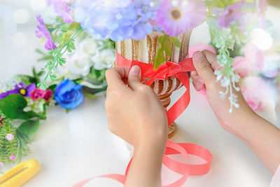 Cropped image of woman tying red ribbon on flower vase