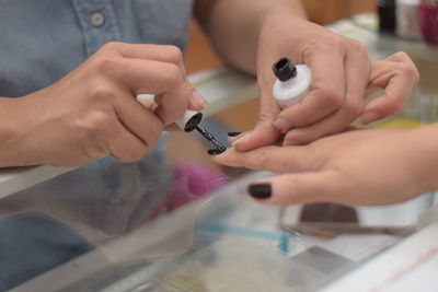 Cropped hand of beautician applying black nail polish on woman fingernails