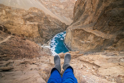 View of human legs wearing rubber boots and stream flowing through rocky mountain