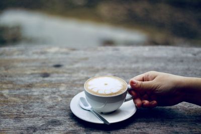 Cropped image of hand holding coffee cup on table