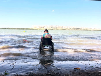 Man sitting at beach against clear sky