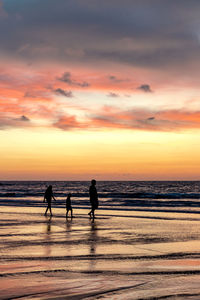 Silhouette people on beach against sky during sunset