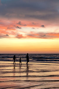 Silhouette family at beach against sky during sunset
