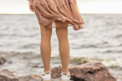 A young woman stands on the rocky shore of the sea. a dress flying in the wind close-up.