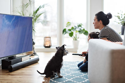 Mother and daughter watching television while sitting with dog on floor at home