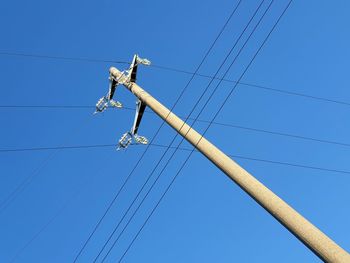 Low angle view of electricity pylon against clear blue sky