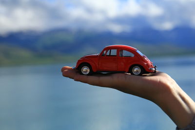 Close-up of hand on red car against sky