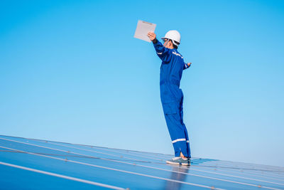 Low angle view of man standing against clear blue sky