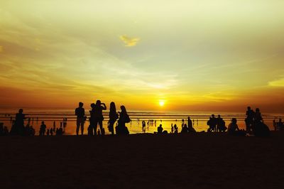 Silhouette people standing on beach against sky during sunset