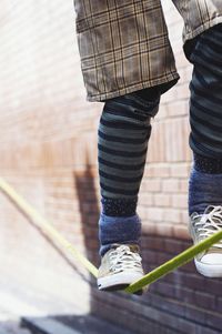 Low section of person walking on tightrope against brick wall