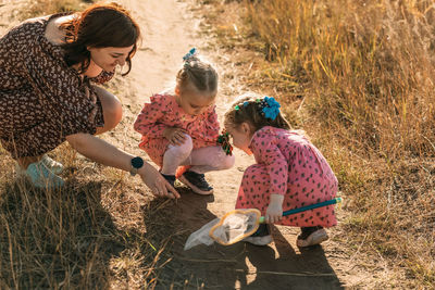 Mom and twin girls catch insects in outdoors with net and study nature with children