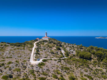 Lighthouse by sea against clear blue sky