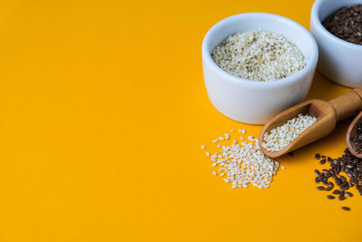 Wooden spoons with sesame and flax seeds lies in a white mortar on a yellow background. healthy eat