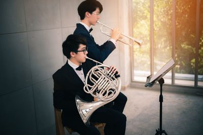Two men playing trumpet and french horn against wall