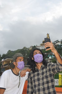 Two male friends with wearing face mask taking selfie together in outside during covid-19 pandemic 