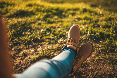 Low section of woman wearing shoes relaxing on field