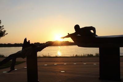 Close-up of silhouette hand against sea during sunset
