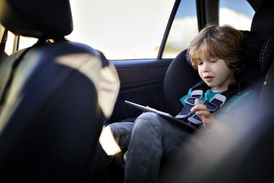 Cute boy using tablet pc while traveling in car