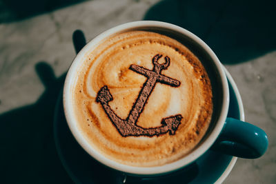 High angle view of anchor on froth art in coffee at table