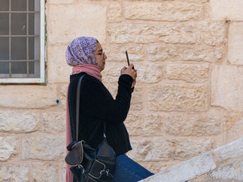 Side view of woman holding umbrella against brick wall