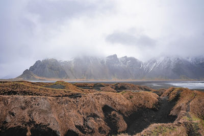 View of grass on black sand against stokksnes cape and vestrahorn mountain