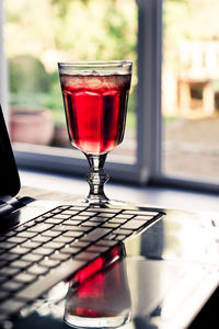 Red drink in glass by laptop on table 