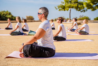 Side view of calm woman with short hair in activewear doing padmasana while sitting on yoga mat during outdoors practice in sunny day