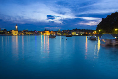 Illuminated buildings by sea against sky at dusk