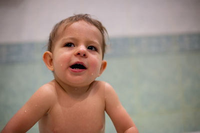  little cute baby while bathing in bath. he looks up with pleased look open mouth.  green bathroom