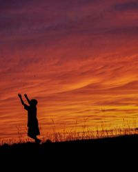 Silhouette man standing on field against orange sky