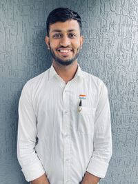 Portrait of smiling young man standing against wall