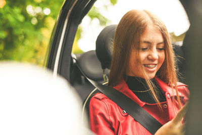 Trendy girl sitting in a car with security belt. smiling teen using smartphone chat with friend.