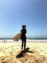 Full length of woman standing on beach against clear blue sky