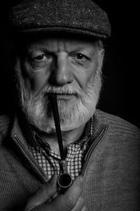 Portrait of senior man with smoking pipe against black background