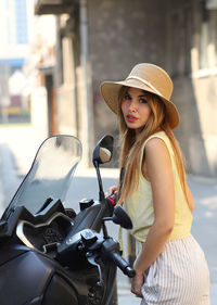 Portrait of young woman standing by motorcycle on road