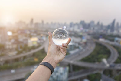 Midsection of man holding crystal ball against sky in city