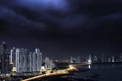 Illuminated city by sea against sky at night