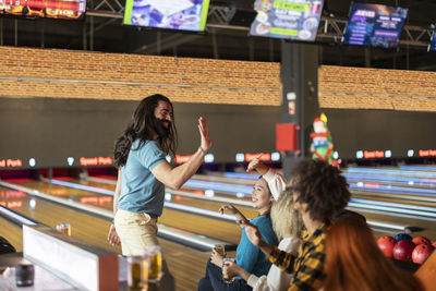 Smiling man giving high five to friend in bowling alley