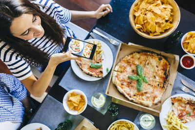 Woman taking cell phone picture of pizza on table