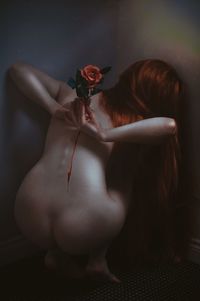 Rear view of young woman holding rose on back against gray background