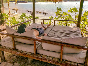 Low section of man sleeping on bed in front of sea, in tropical island 