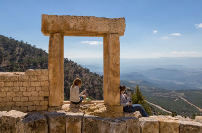 Women sitting on old ruin against mountains