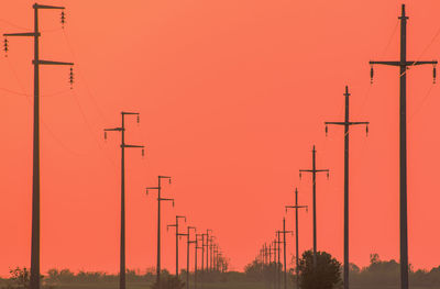 Low angle view of silhouette electricity pylon against orange sky