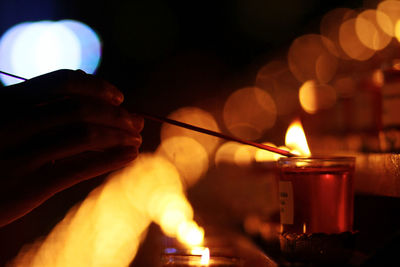 Close-up of hand holding incense over lit candle