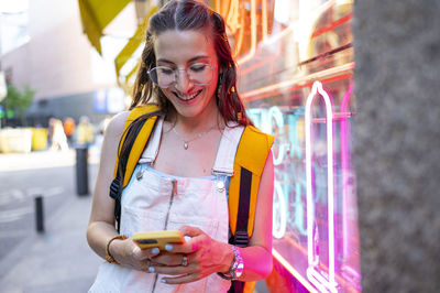 Soft focus of happy female smiling and browsing cellphone on sunny morning on city street