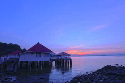 House by sea against sky at sunset