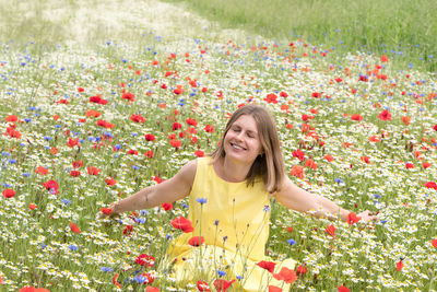 A beautiful young blonde woman in a yellow dress stands among a flowering field