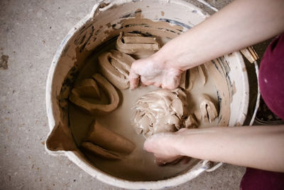 High angle view of hands holding clay in container