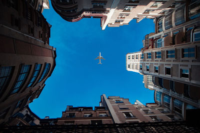 Low angle view of airplane flying over buildings against blue sky